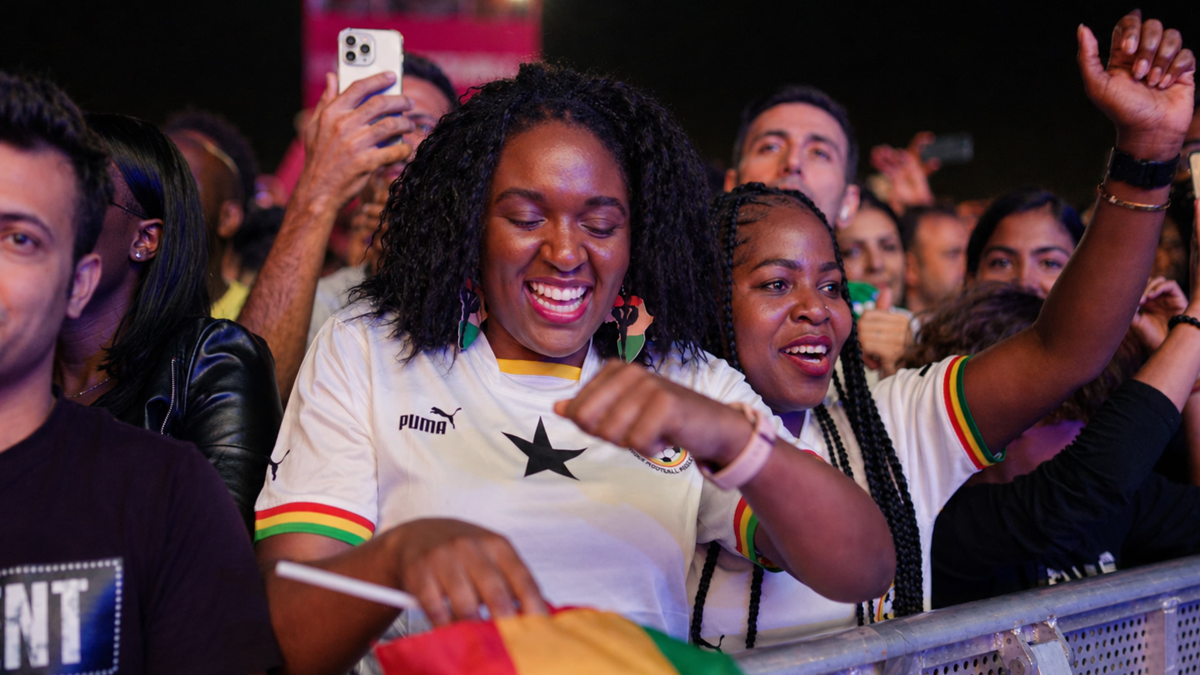 Fans in Ghana jerseys celebrating in the crowd at the FIFA Fan Festival